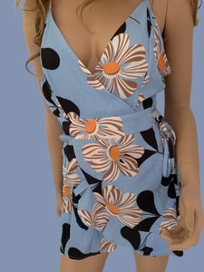 Periwinkle blue romper with big beautiful white flowers is made of lightweight breezy textured crepe material. Has adjustable shoulder straps with a V-neck and fitted lined bodice. It has a high waist bottom with wrap around design front. Brighten up your summer wardrobe with this fun romper. No stretch fabric. 